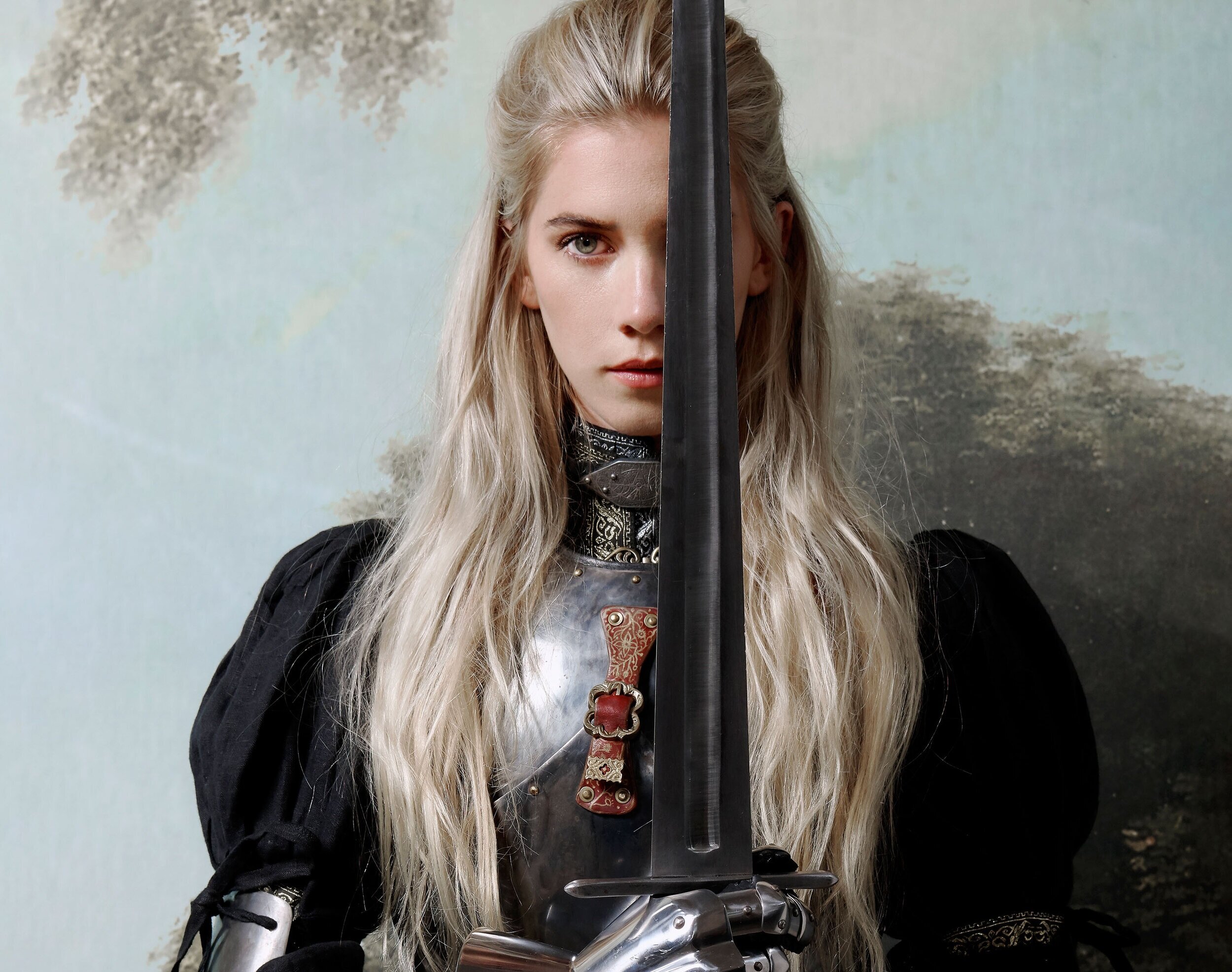 Woodes wears a suit of armour and holds a sword that covers half her face